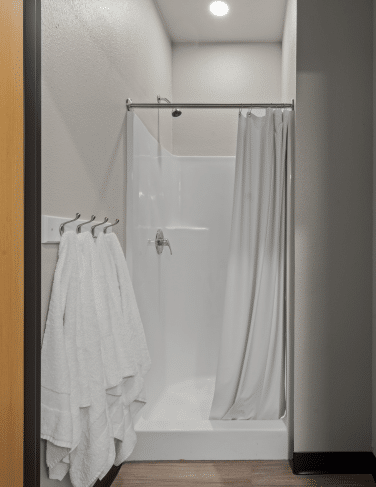 Shower stall with a white tub and light gray curtain; three white towels hang on a rack to the left in a bathroom.