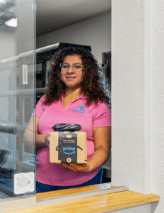 Delivery person with curly hair at a service window, holding a small Amazon Prime package for pickup or delivery.