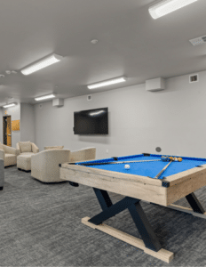 Pool table with blue felt and billiard balls in a lounge area of a recreation room.